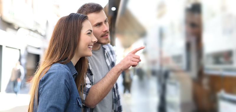 Un homme et une femme qui regarde une vitrine d'agence immobilière.