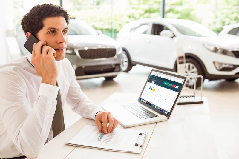 Homme au téléphone dans une concession devant son ordinateur ouvert sur l'espace client Contact manager +